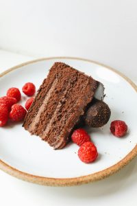 Close-up of a chocolate cake slice on a ceramic plate, garnished with fresh raspberries.